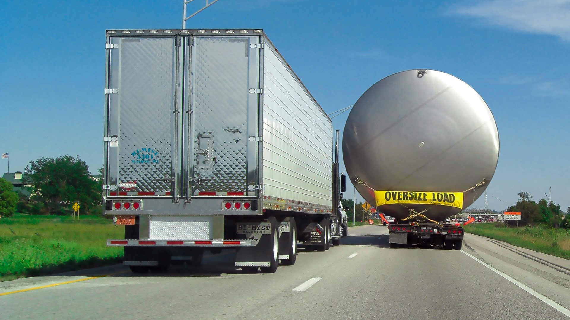A large pressure vessel chained to a lowboy trailer beside port cranes, ready for export loading